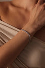 RITI heart-shaped cubic zirconia tennis bracelet with bezel setting worn on a woman's wrist in a beige top.
