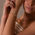 RITI gold tennis bracelet featuring heart-cut cubic zirconia stones in a bezel setting worn on a woman's wrist.