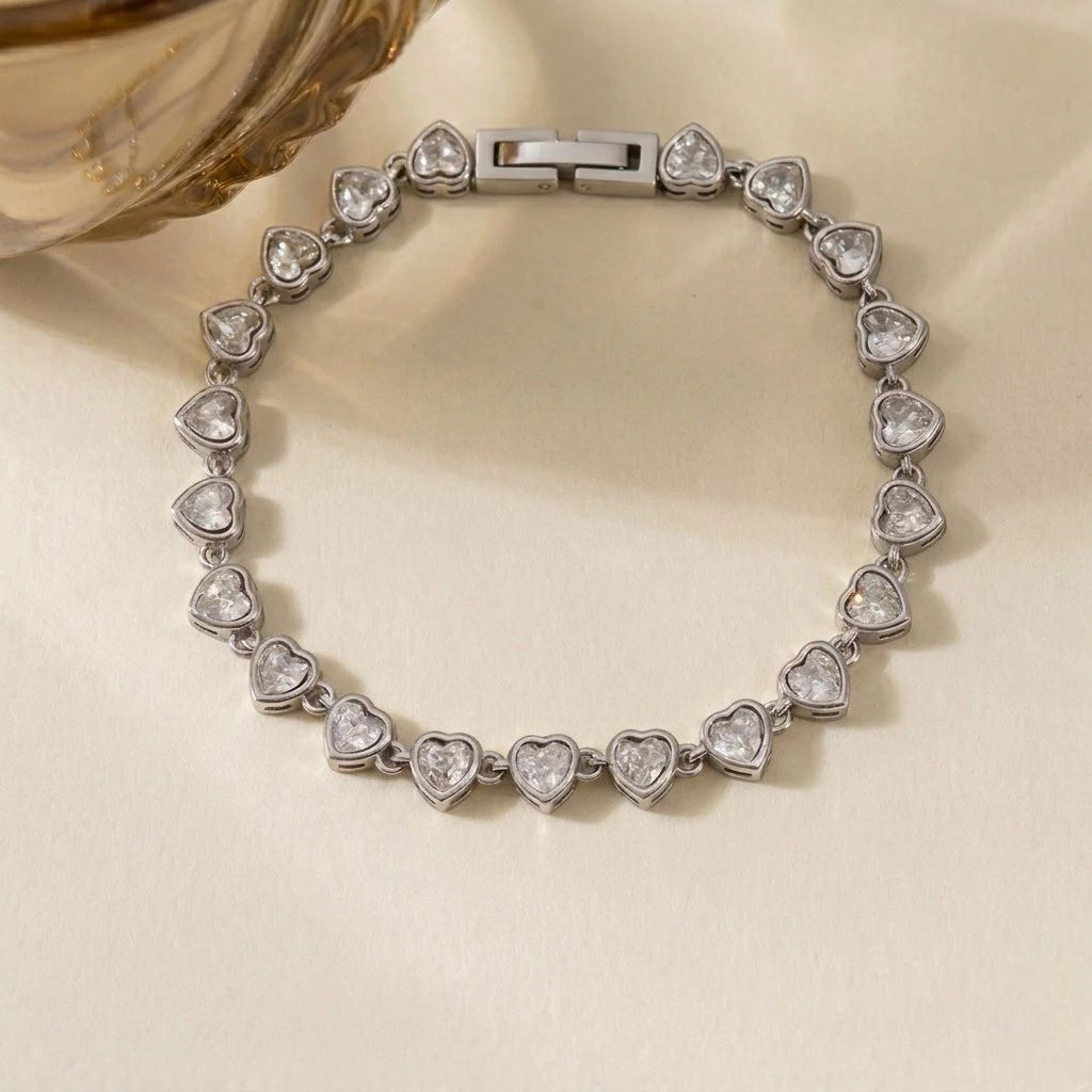 RITI heart tennis bracelet featuring clear cubic zirconia stones in a silver-tone bezel setting on a neutral surface.